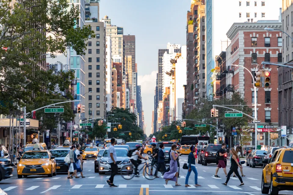 Pedestrians crossing a busy crosswalk on New York City street with tall buildings in background